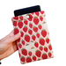 A hand holding a  Kindle sleeve with snap to protect Kindle e-readers made with a pink back ground with red and white strawberries.